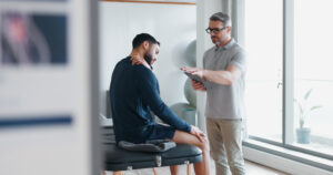 Physiotherapy, tablet and shoulder pain with people in clinic for rehabilitation, healthcare or consulting. Support, medical and chiropractor with man and athlete for healing, advice or report